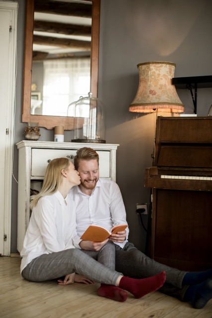 liebevolles Paar sitzt auf dem boden neben einem Klavier und er liest aus einem Buch. Das E-Book von Michael Lahme Coaching ist eingetroffen.