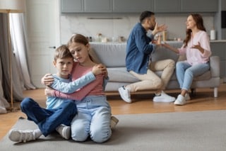 Kommunikation nach Trennung mit Kind. Geschwisterpaar im Vordergrund beschützen sich gegenseitig beim Streit der Eltern im Hintergrund.