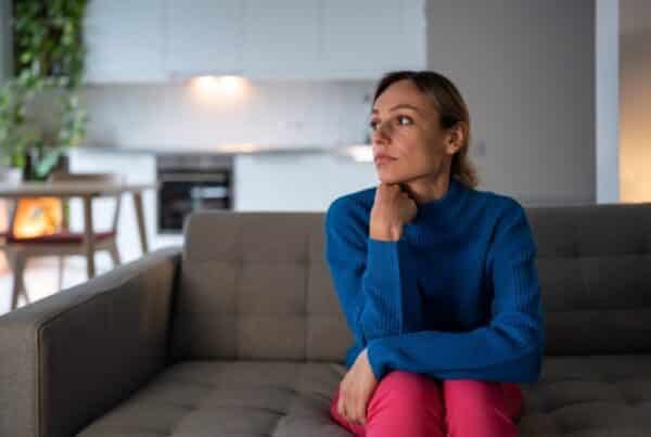 Frau sitzt allein am Fenster – Nähe fällt ihr schwer