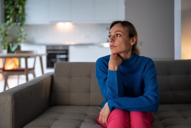 Frau sitzt allein am Fenster – Nähe fällt ihr schwer