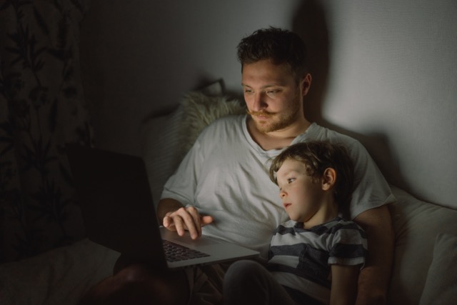 Loyalitätskonflikt bei Kindern: Junge sitzt abends wach auf dem Sofa neben seinem Vater